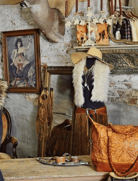 A western boutique corner: fringed leather, a felt hat on a mannequin, and a tooled leather bag on a wooden counter